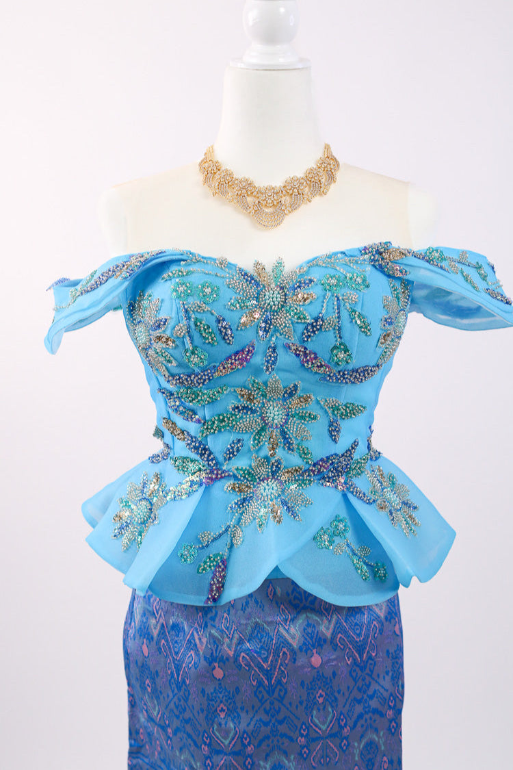 Blue embroidered top and skirt set on a mannequin with a necklace against a white background