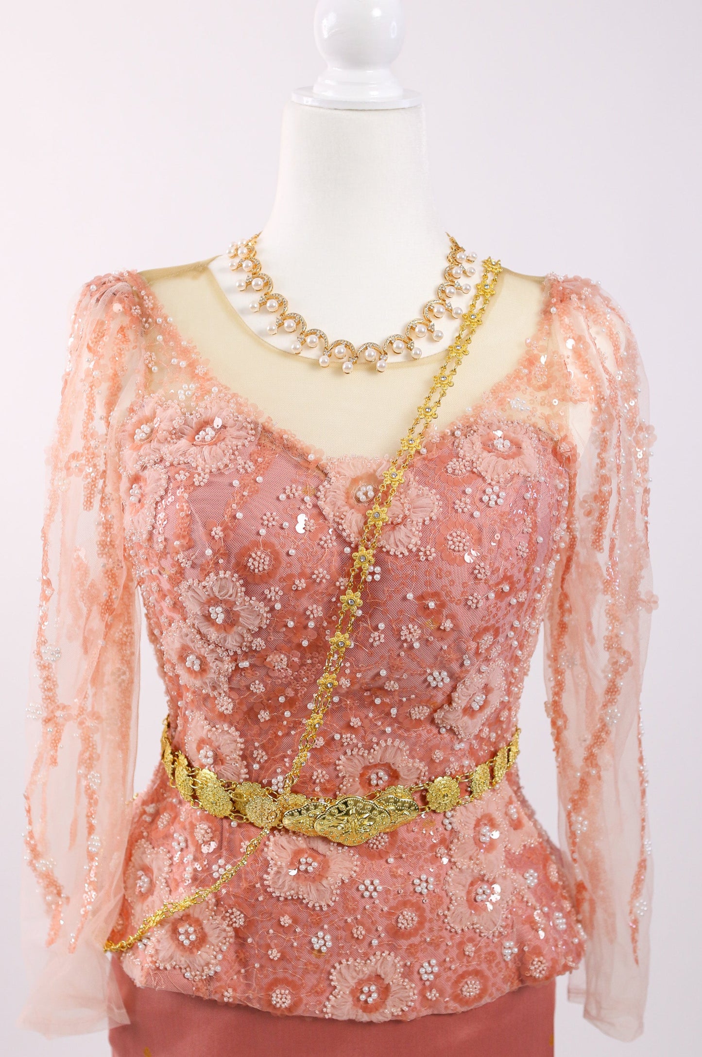 Peach-colored blouse with floral patterns and gold accents on a mannequin against a white background