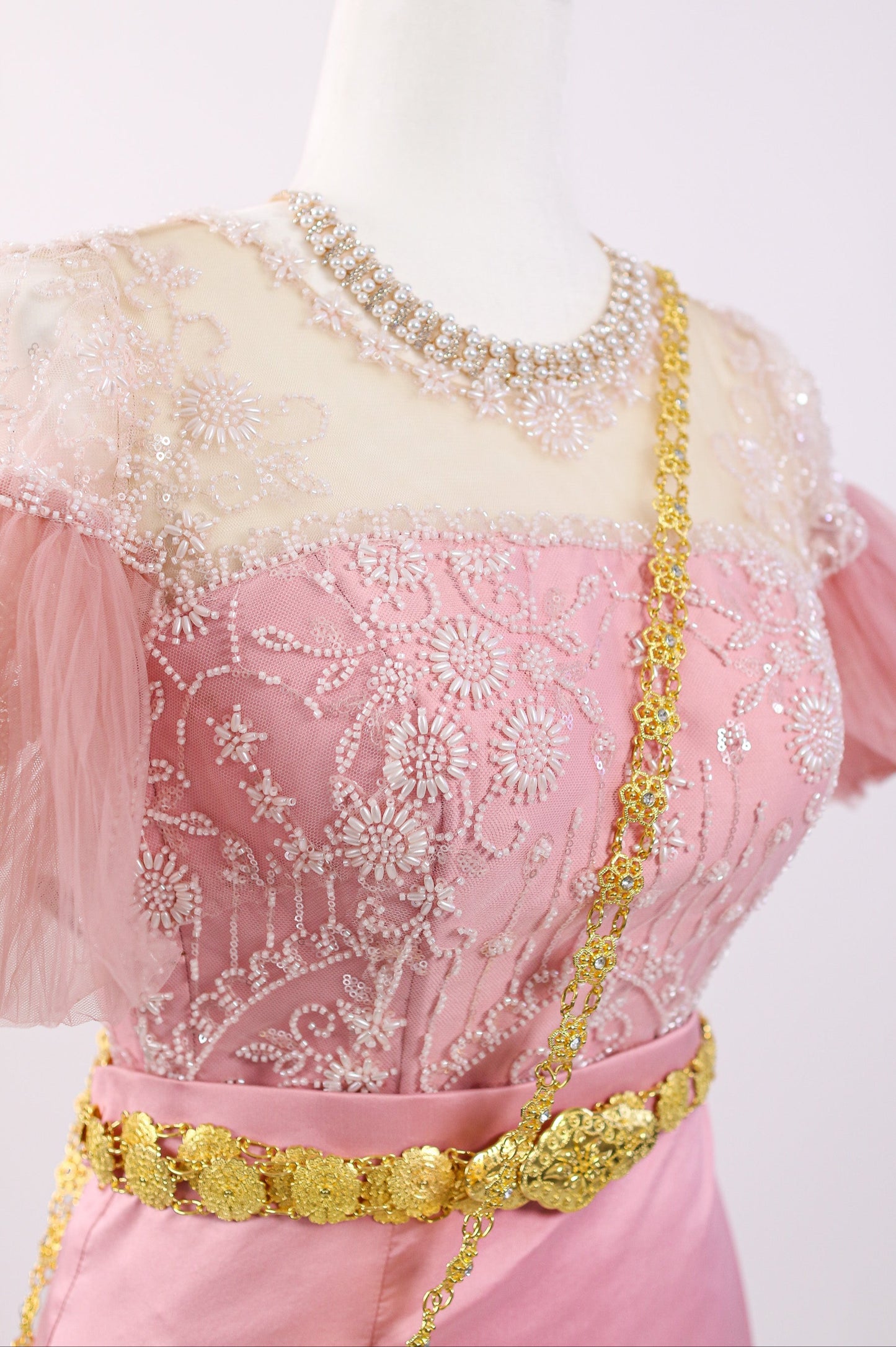 Mannequin wearing a pink dress with gold embellishments on a white background