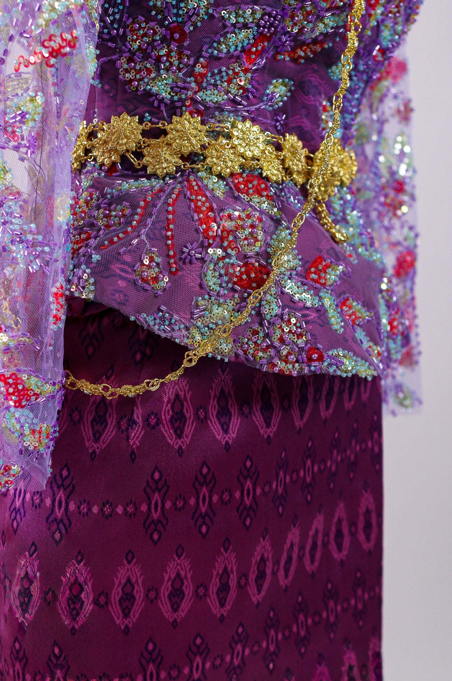 Decorative purple garment with floral patterns and a gold belt on a light gray background