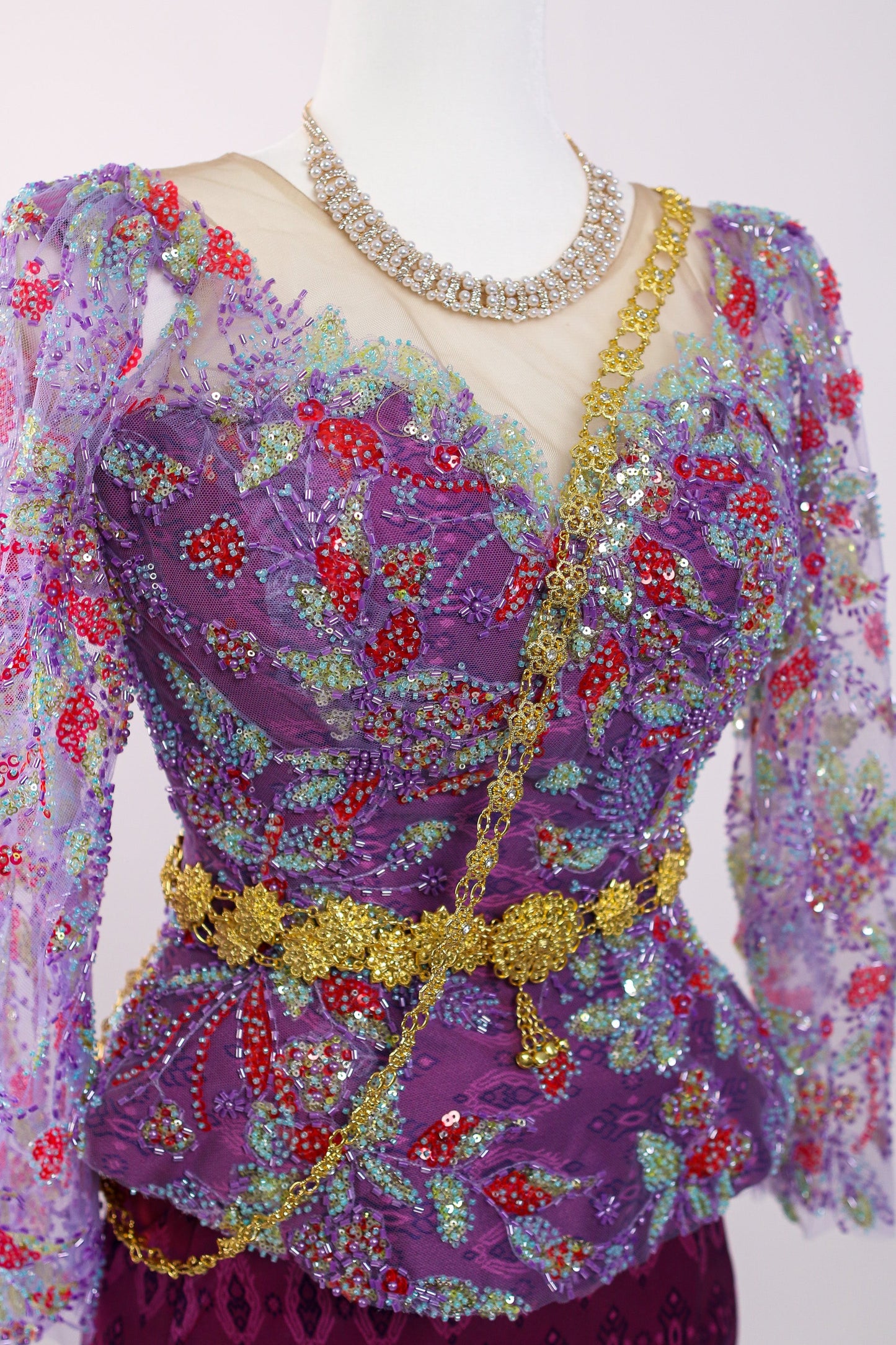 Decorative purple top with floral patterns and a gold belt on a mannequin against a white background