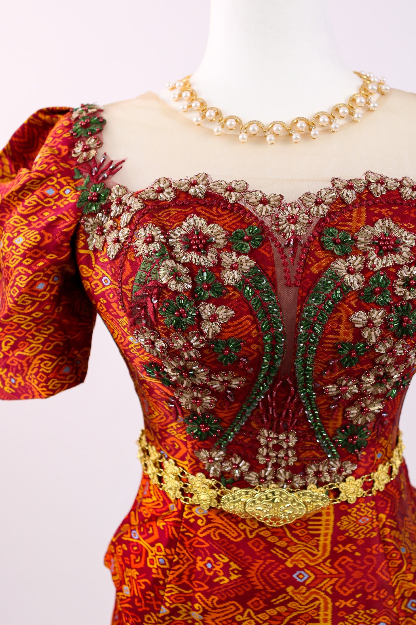 Decorative red and gold garment on a mannequin with intricate patterns.