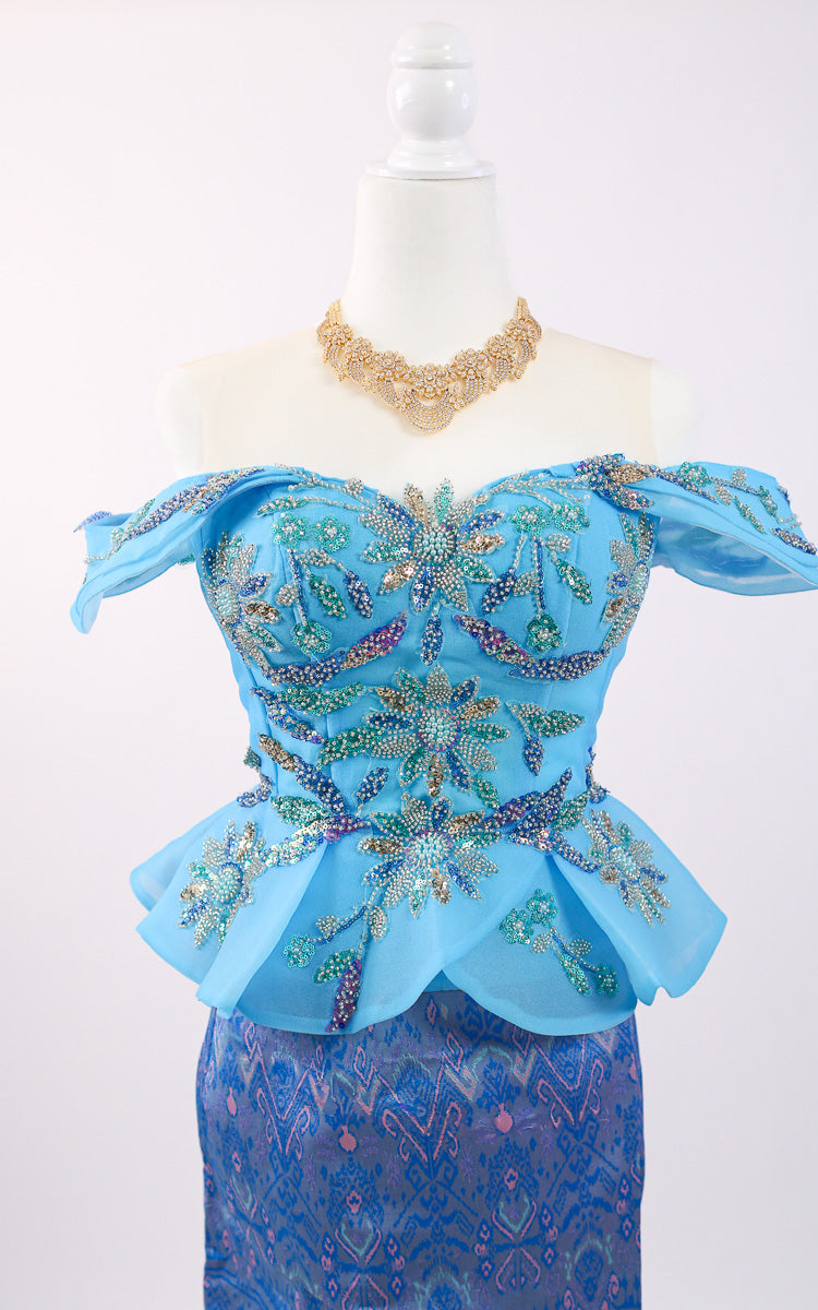 Blue embroidered top and skirt set on a mannequin with a necklace against a white background