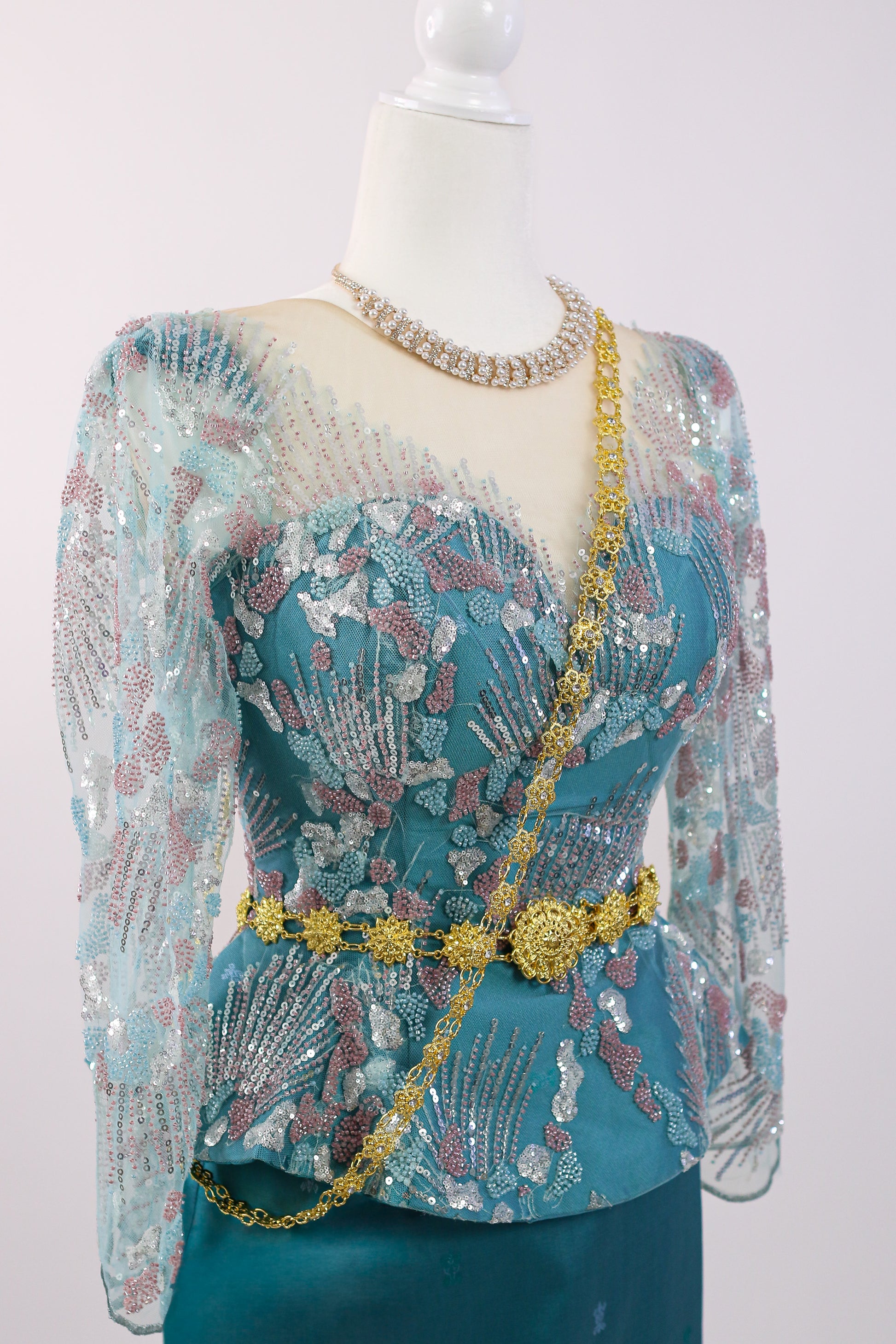 Mannequin wearing a teal dress with floral patterns and gold accents on a white background