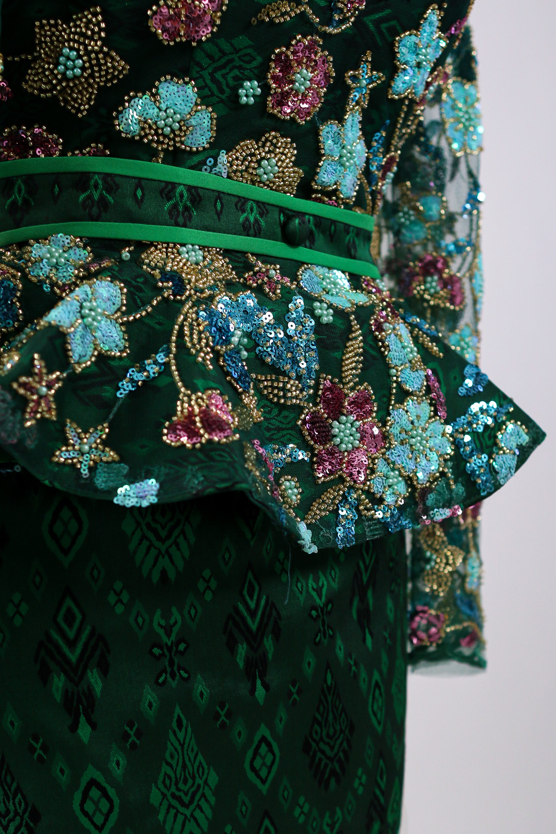 Close-up of a green embroidered garment with floral patterns on a white background
