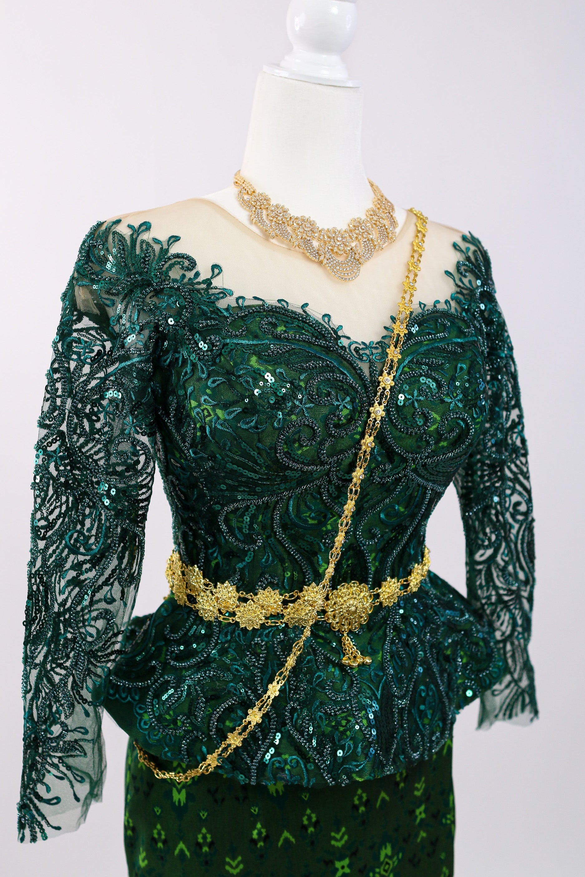 Green lace dress with gold accents on a mannequin against a white background