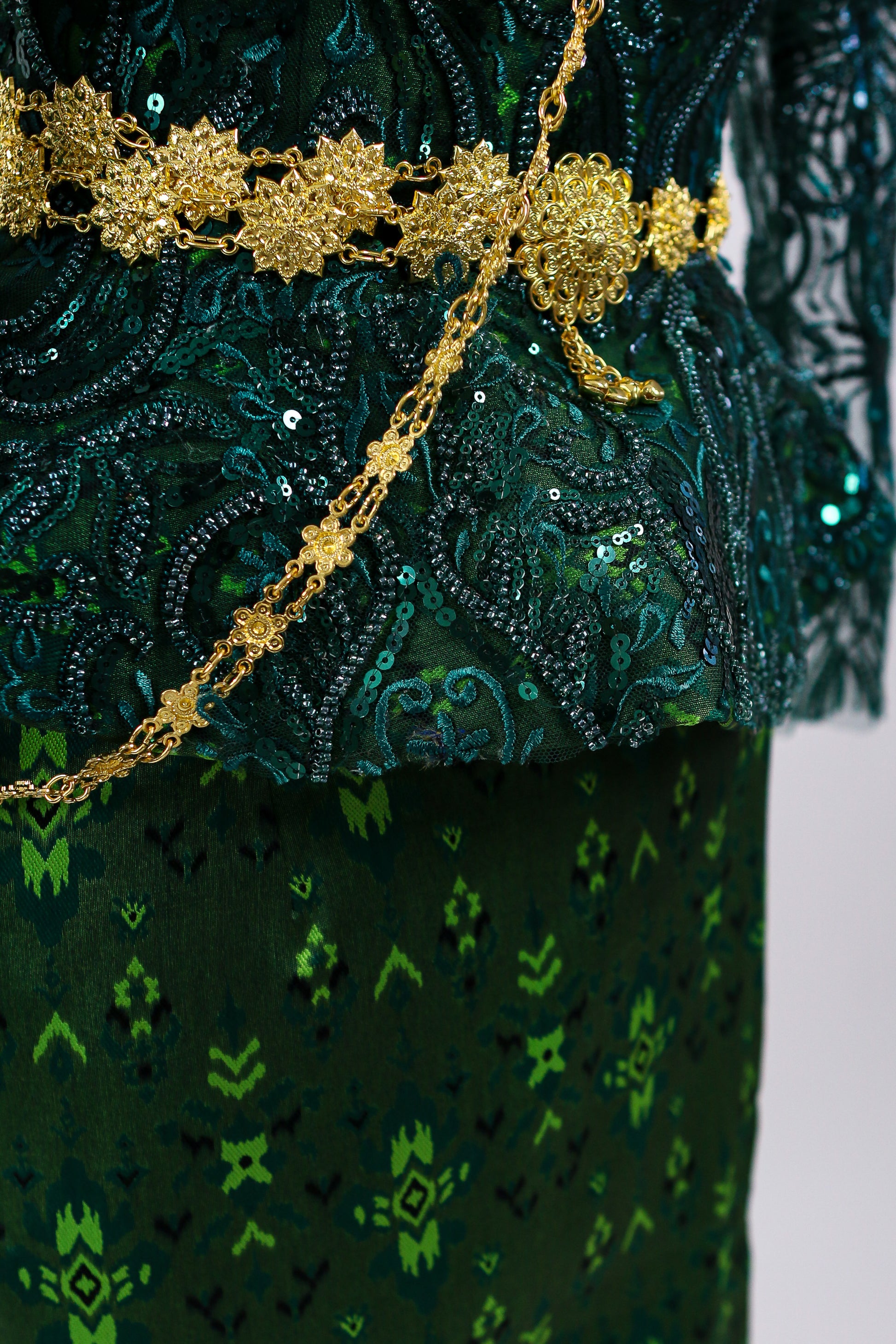 Close-up of a green embroidered garment with gold detailing on a white background
