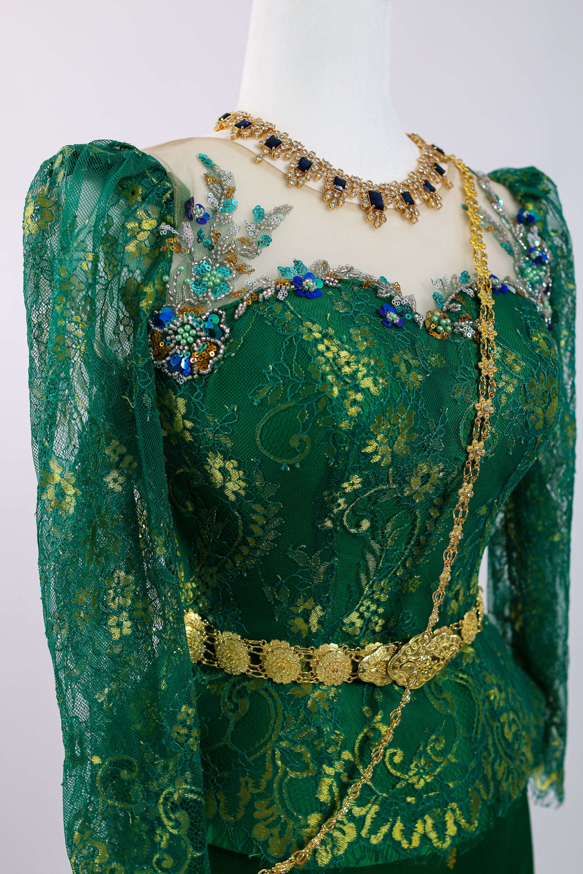 Green embroidered garment with gold and blue embellishments on a mannequin against a white background