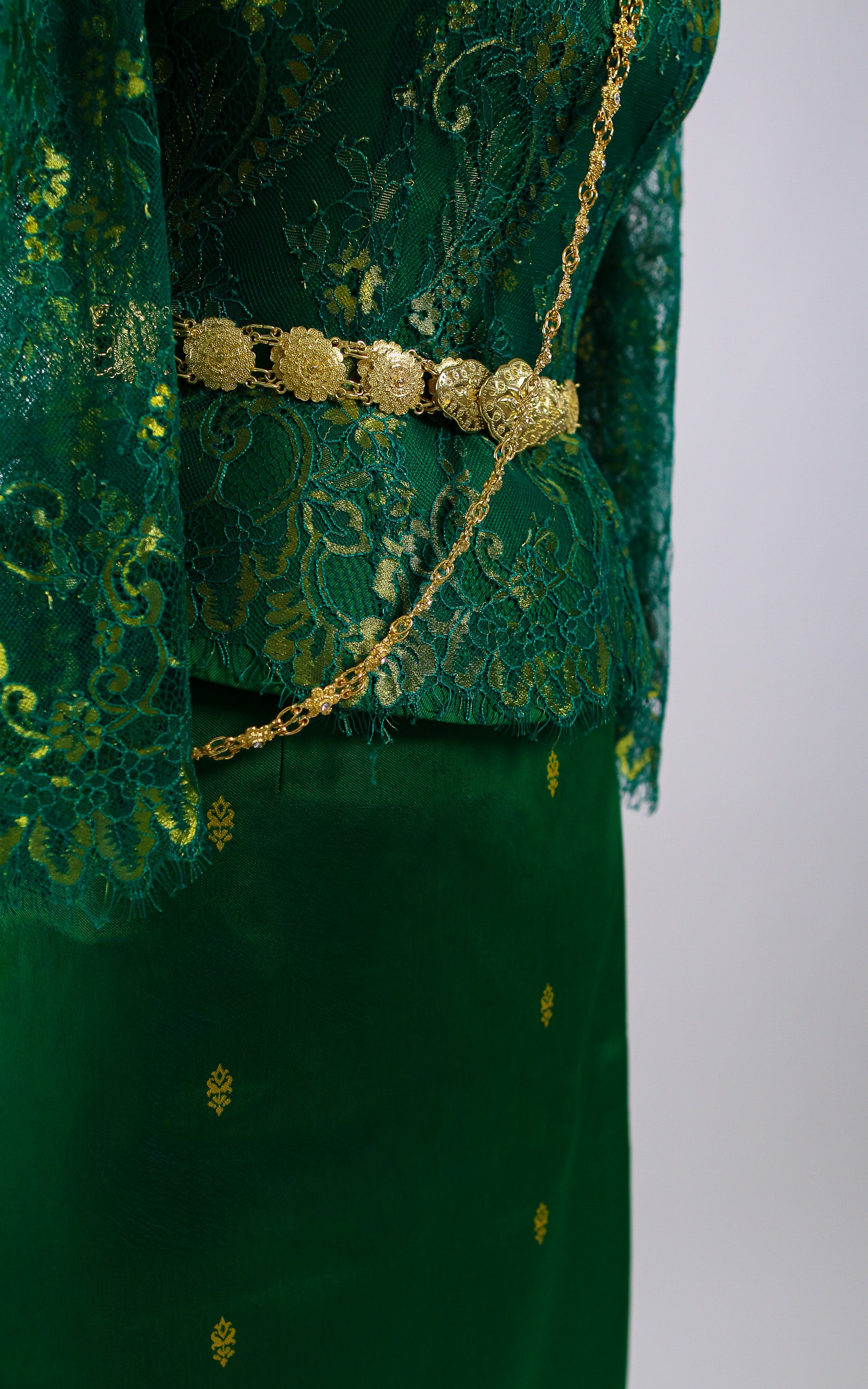 Green embroidered garment with a gold belt on a white background