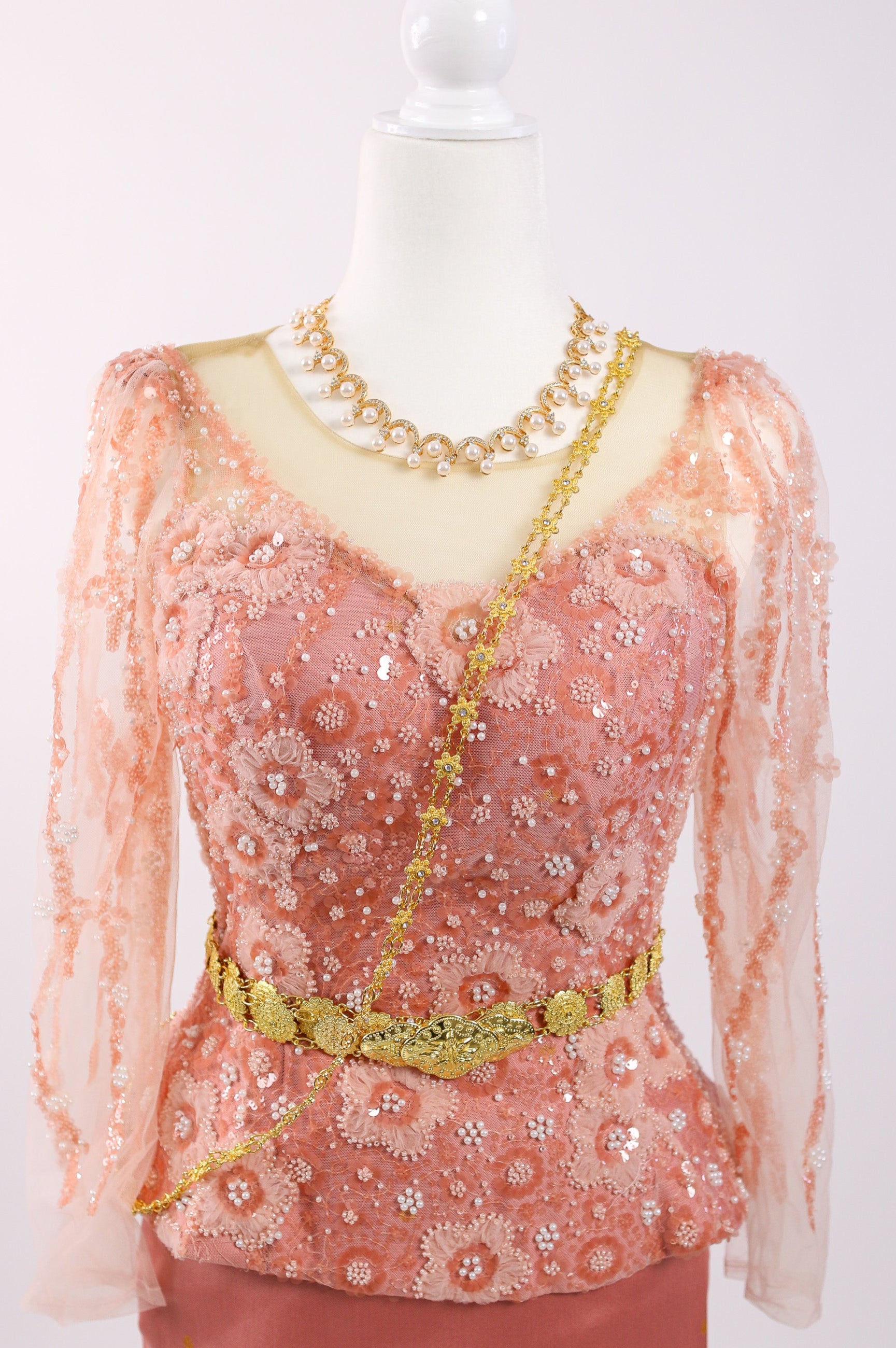 Peach-colored blouse with floral patterns and gold accents on a mannequin against a white background