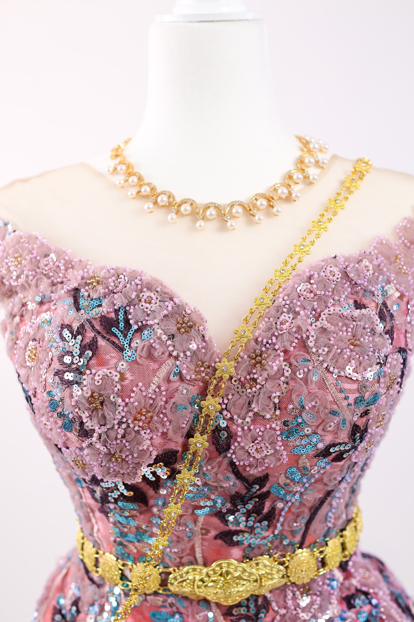 Mannequin wearing a pink dress with floral patterns and gold accents on a white background