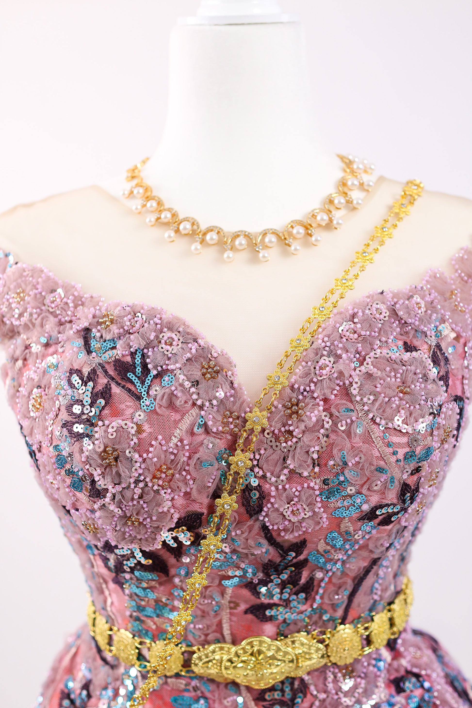 Mannequin wearing a pink dress with floral patterns and gold accents on a white background