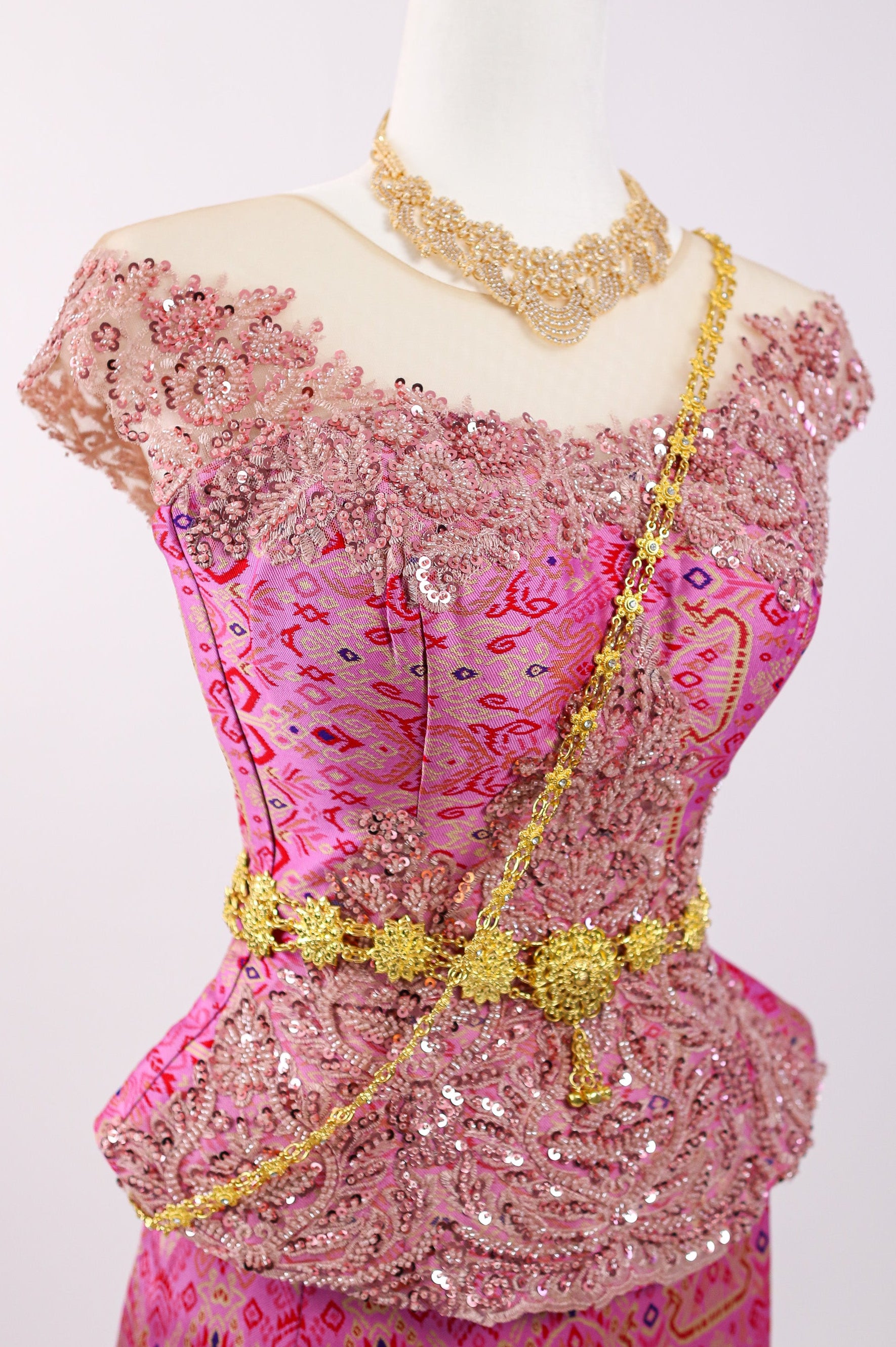 Pink embroidered top with gold details on a mannequin against a white background