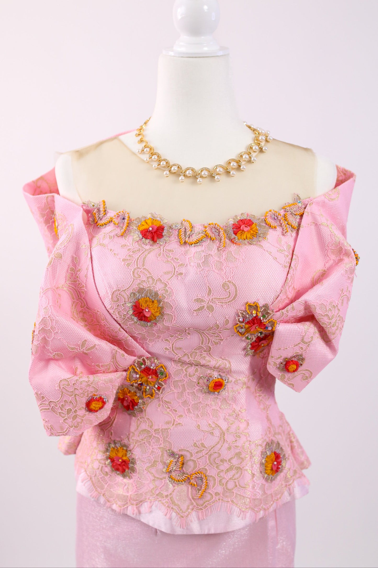 Pink blouse with floral embroidery on a mannequin against a white background