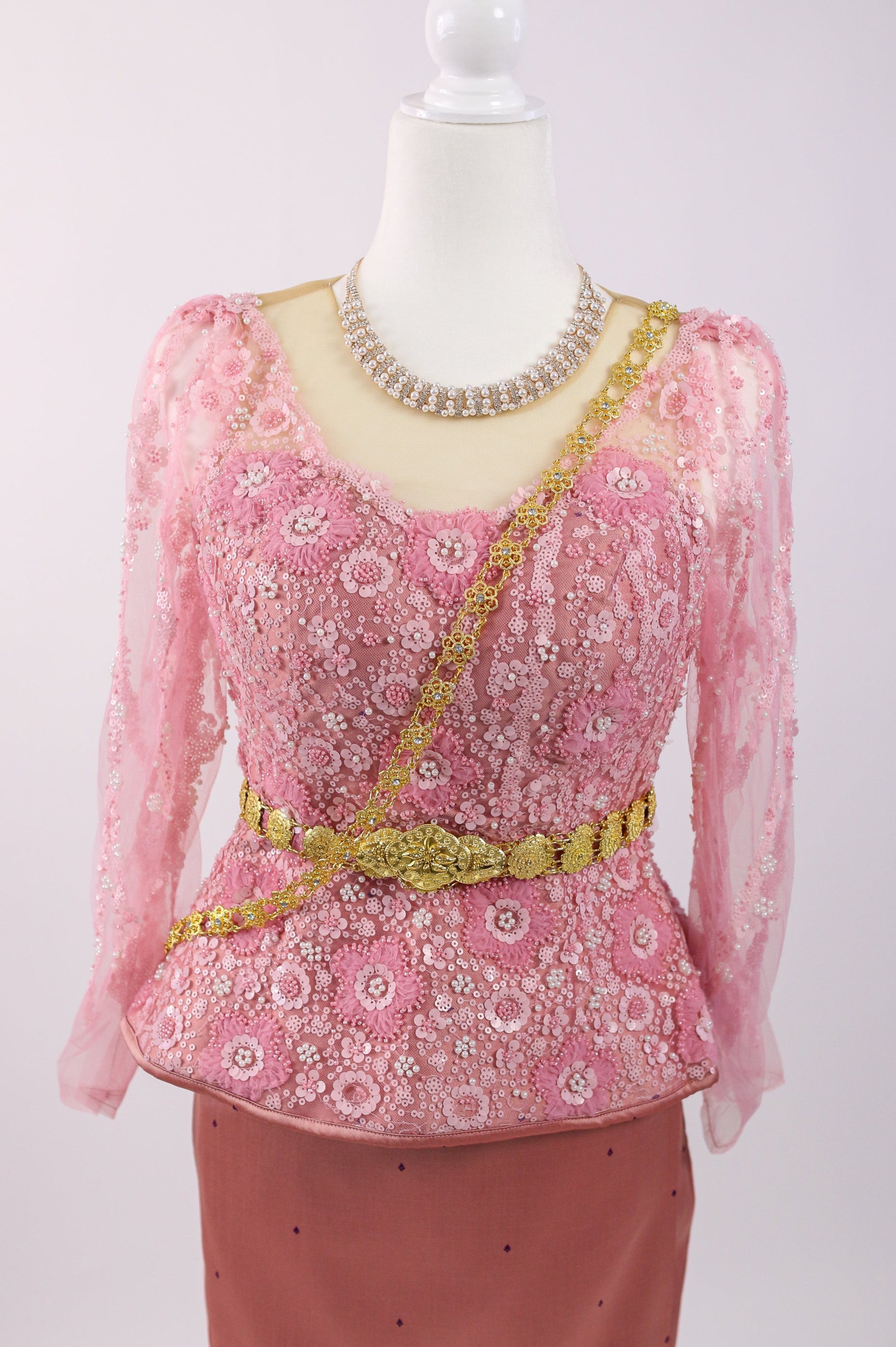 Mannequin wearing a pink embroidered top with a necklace on a white background