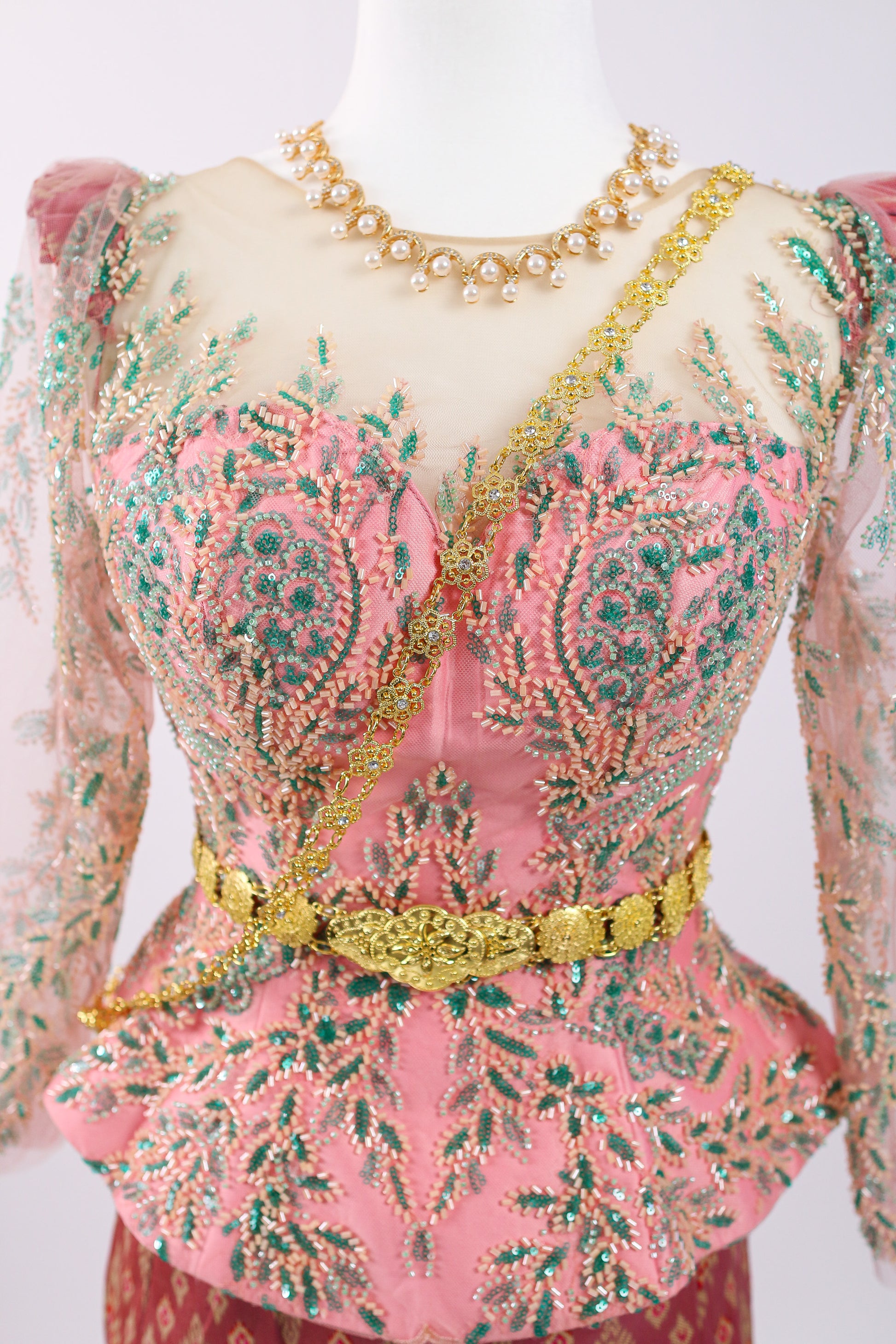 Pink embroidered blouse with gold detailing on a mannequin against a white background