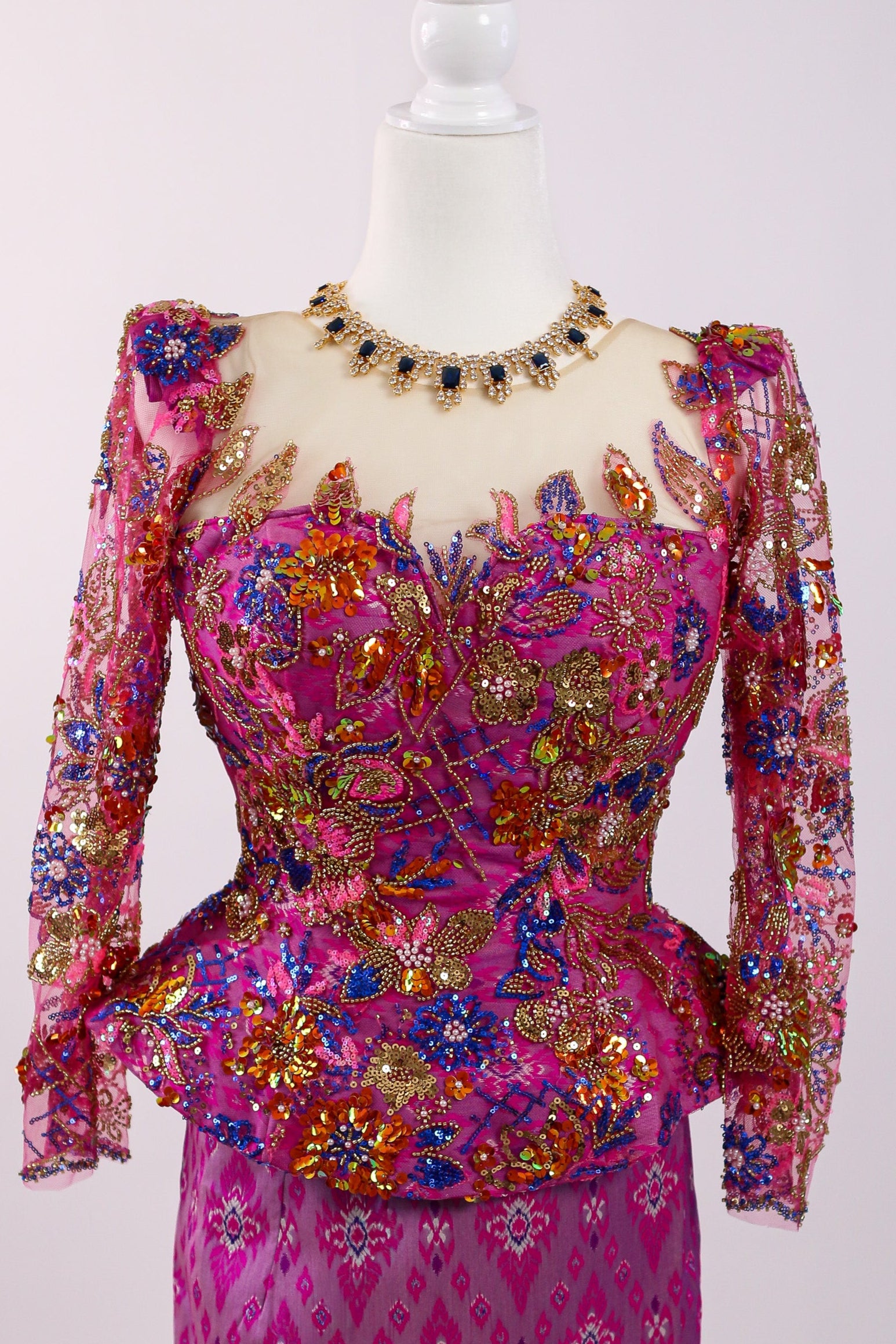 Mannequin wearing a vibrant pink and multicolored dress with intricate patterns on a white background