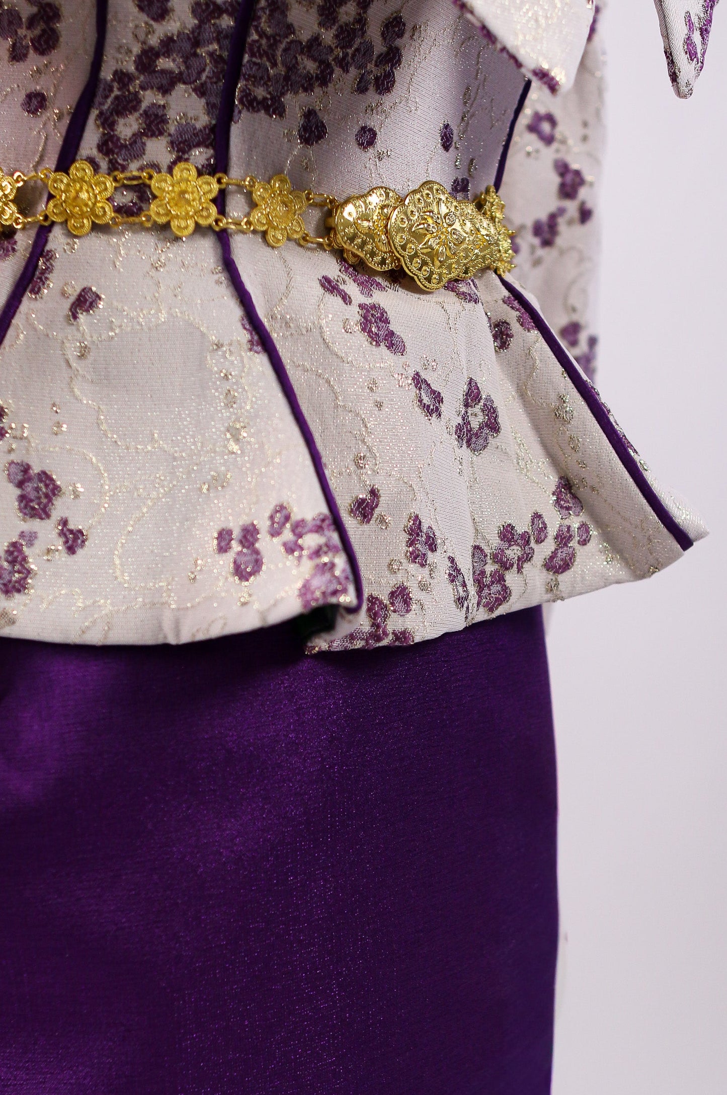 Close-up of a traditional outfit with a gold belt and floral patterns on a white background
