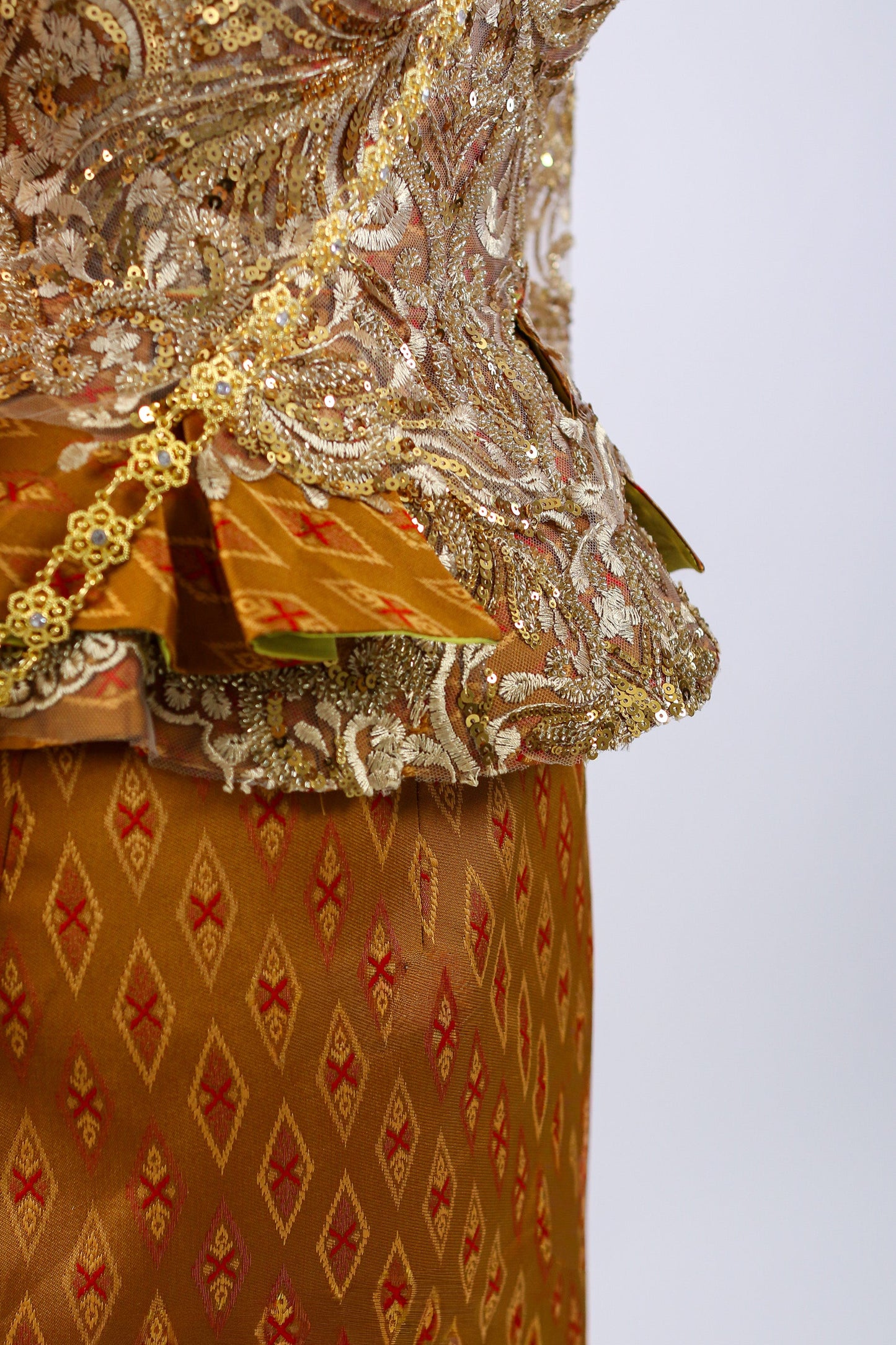Close-up of a traditional embroidered garment with gold and red patterns on a plain background